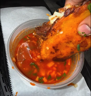Quesabirria taco being dipped in red consomé