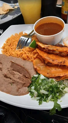 Quesabirria tacos plated with consomé, rice and beans